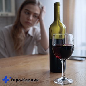 Девушка расстроенно сидит перед бутылкой вина